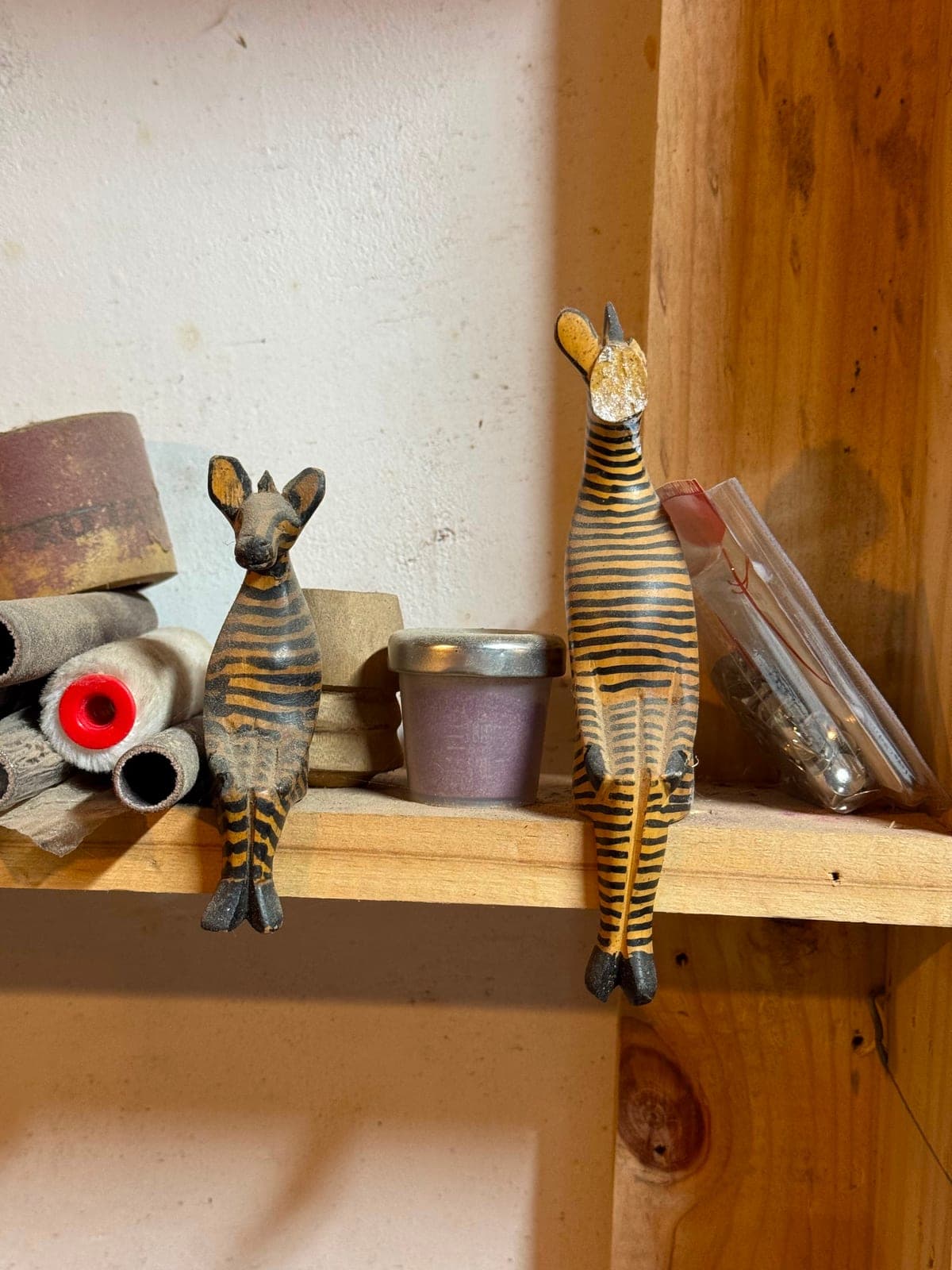 Two small hand-carved striped animal figures standing on a wooden workshop shelf beside flute parts