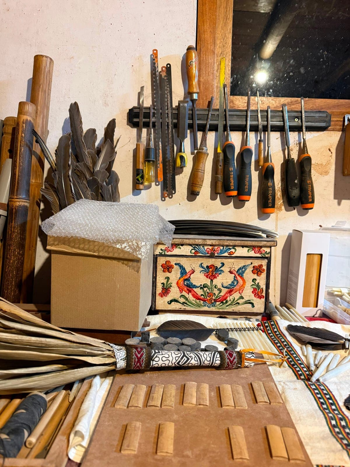 A rack of files and chisels above a workbench, with a painted box of folk birds and rows of flute parts laid out below
