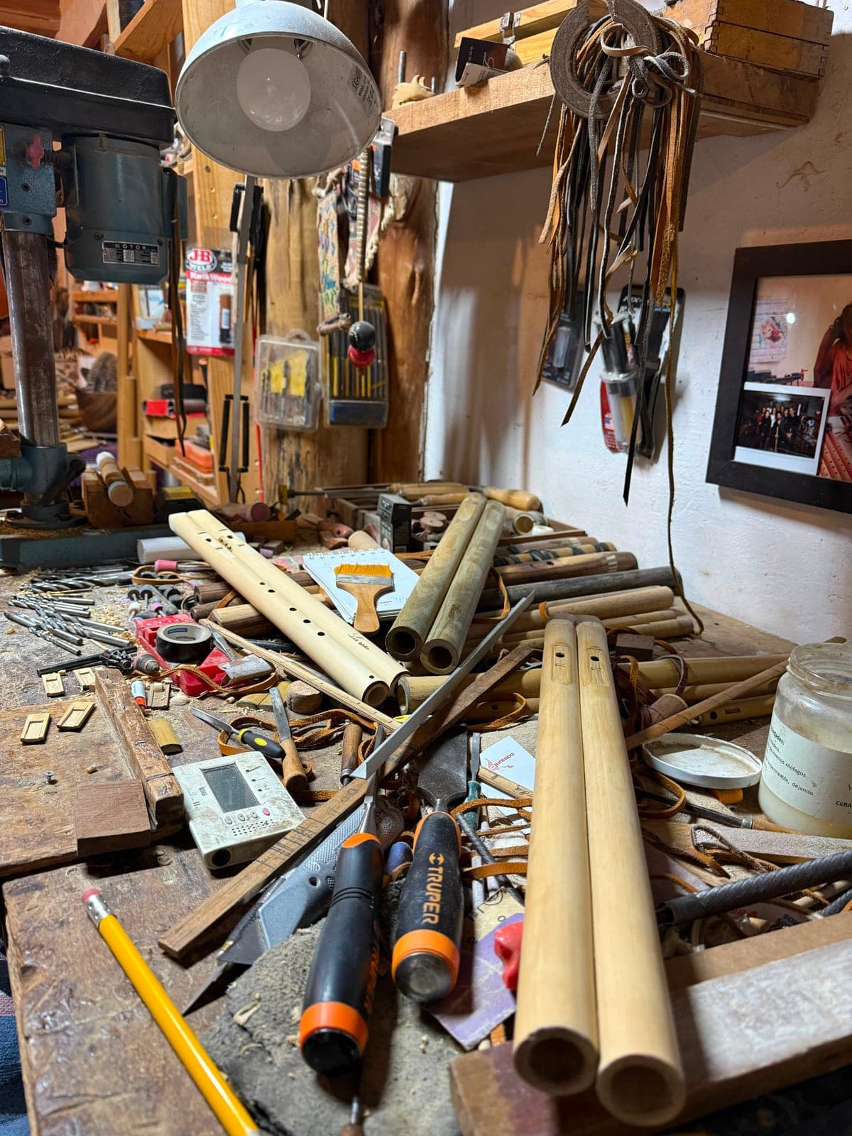A cluttered workbench in Omar's flute workshop, strewn with bamboo flutes, hand tools, and a work lamp