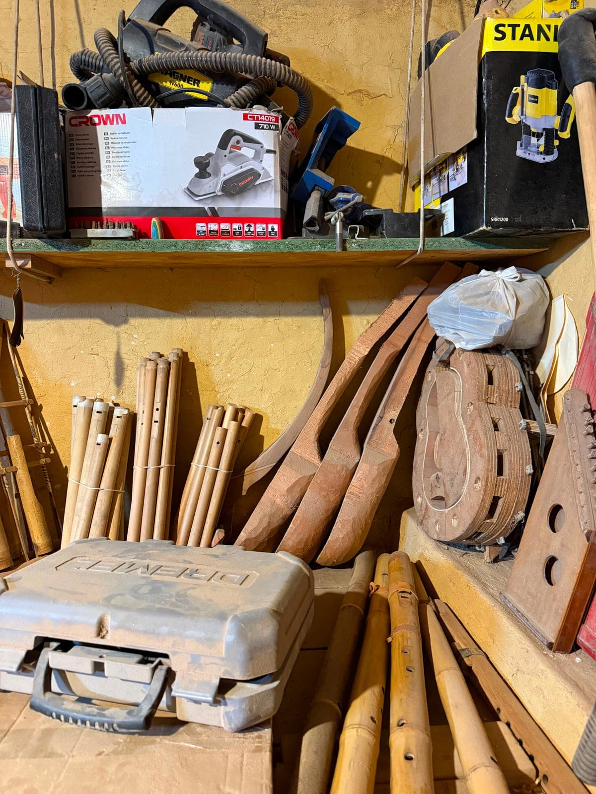 A workshop shelf stacked with wooden flute blanks and hand tools, power tools resting on the shelf above