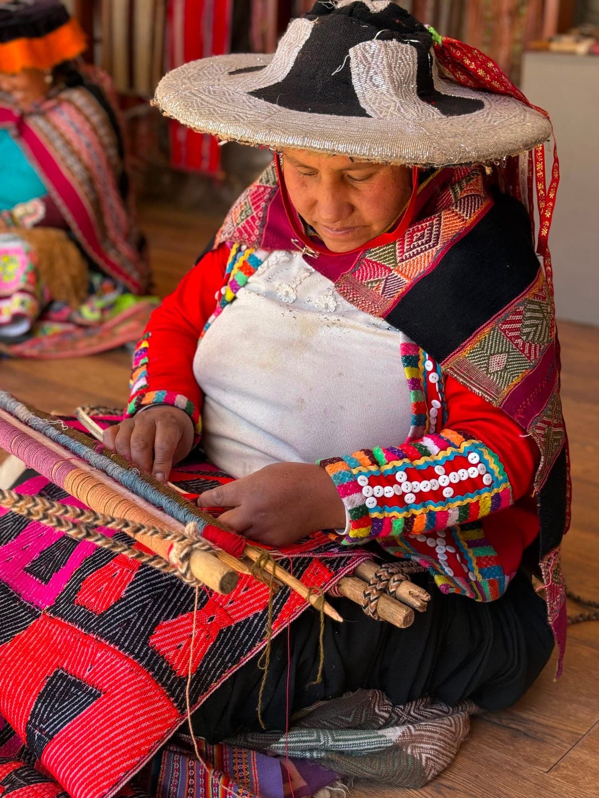 A Peruvian woman in bright traditional dress weaving textiles on a backstrap loom