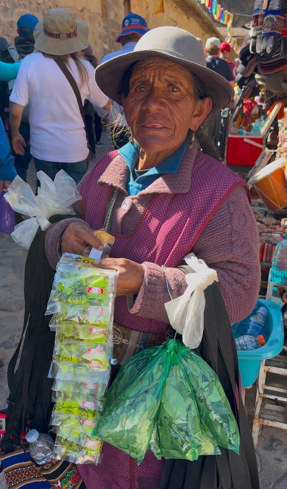 An older Peruvian woman selling coca candy and coca leaves at a busy market lined with artisan stalls