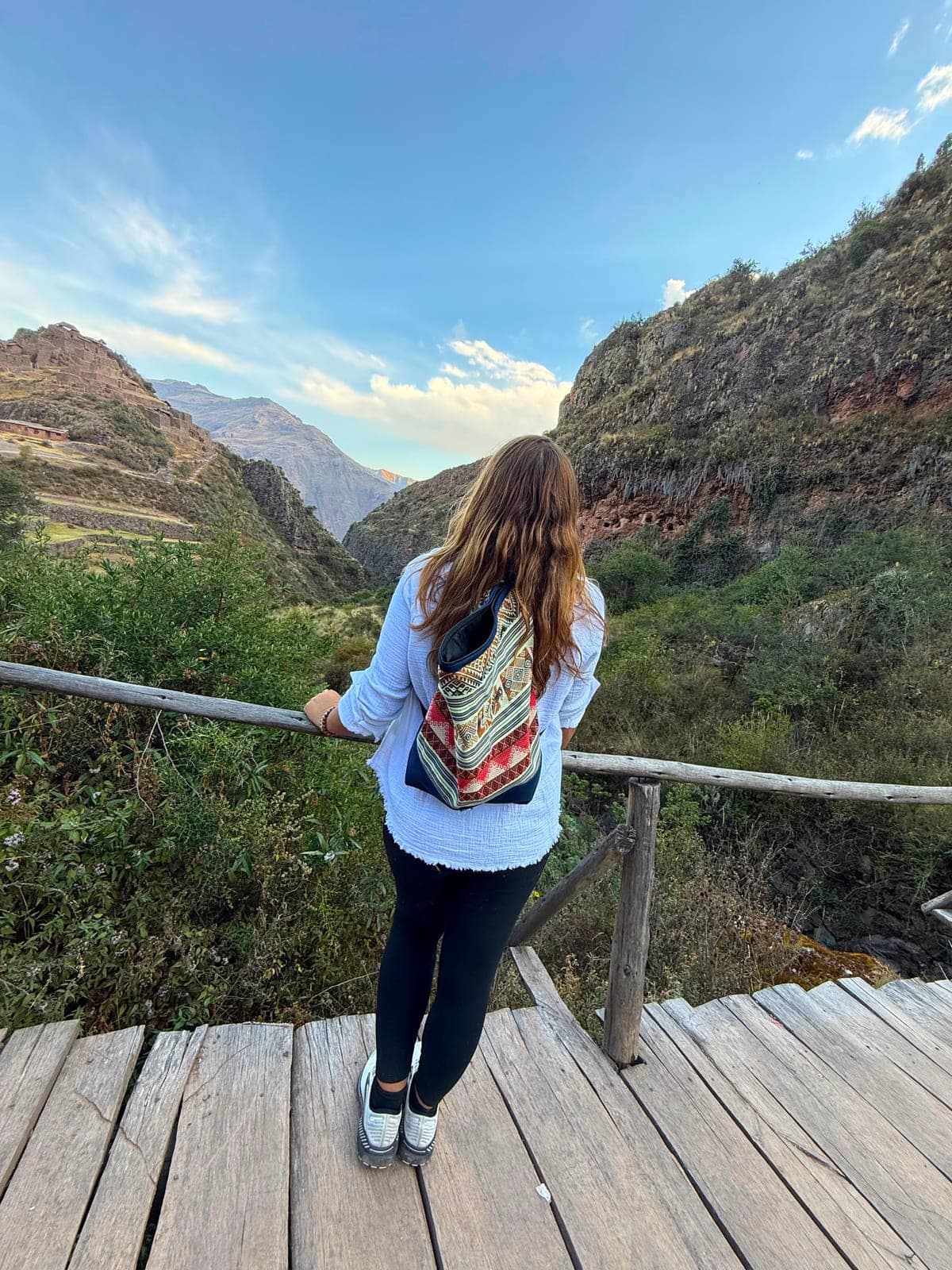 Sarah standing on a wooden bridge with her new colorful Peruvian backpack, gazing at the ruins and mountains ahead