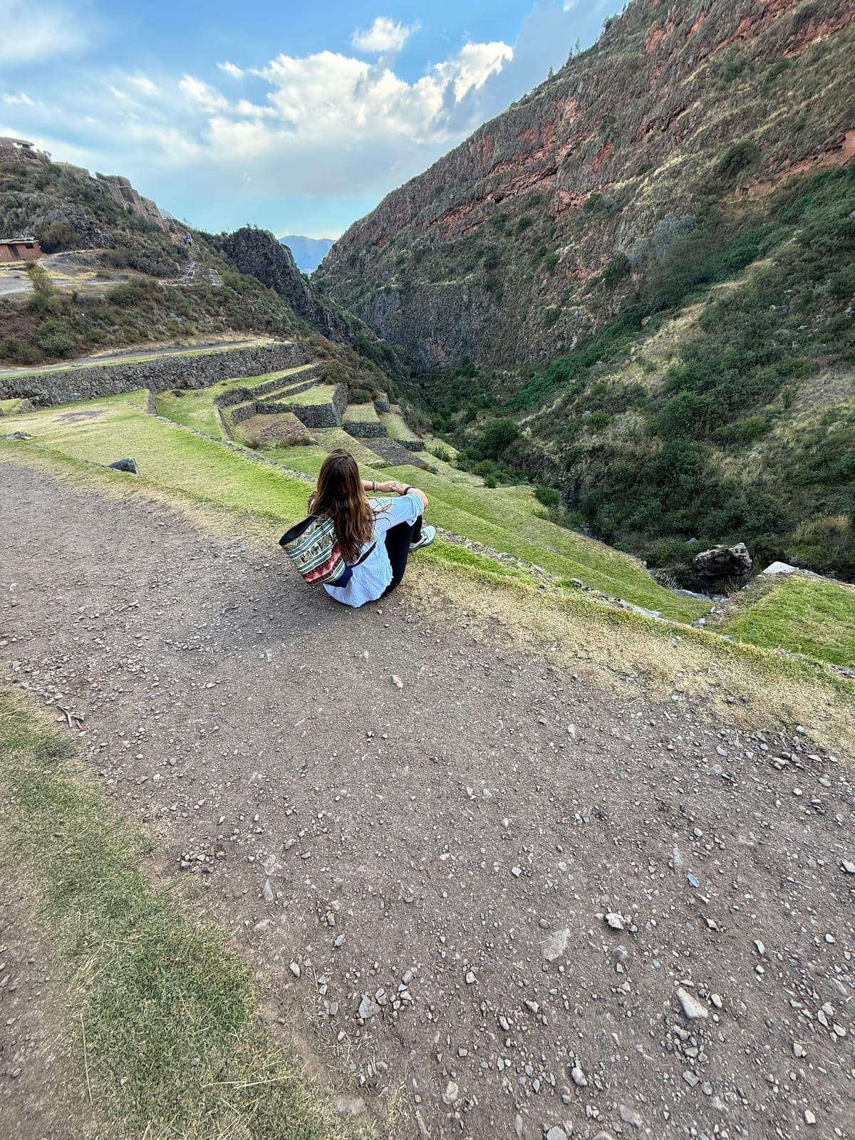 Sarah sitting at the edge of a path with a colorful woven backpack, looking out over the terraced gorge