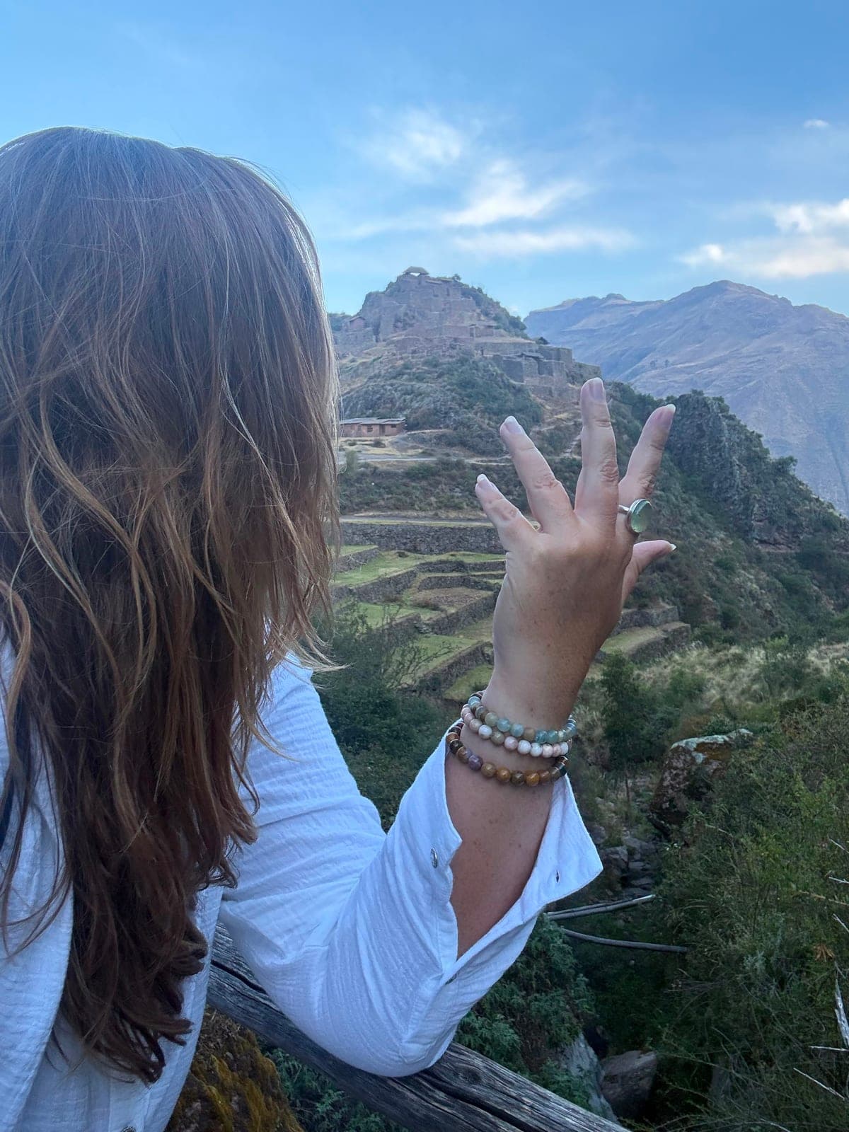 Sarah reaching a hand out toward the Inca citadel perched on the mountain across the valley