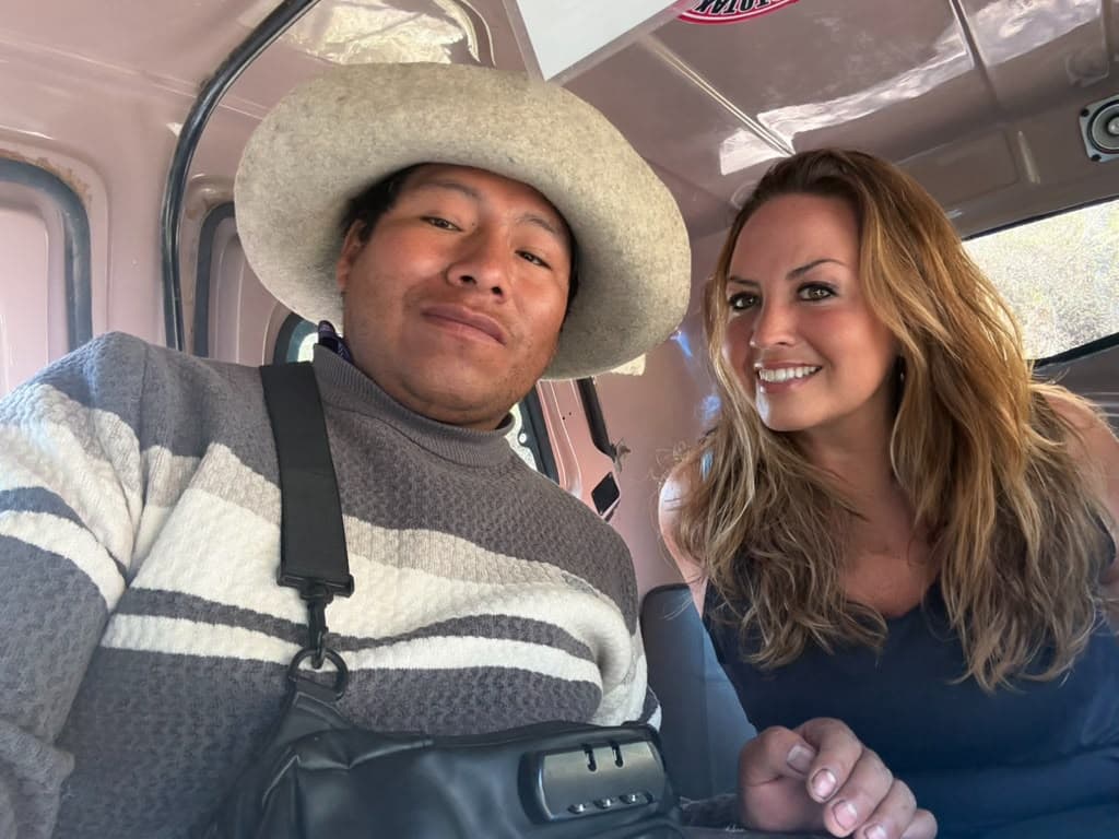 Sarah smiling in the back of a shared colectivo beside a man in a wide straw hat