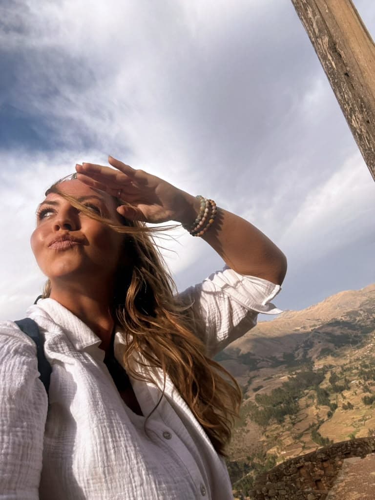 Sarah shielding her eyes against a bright sky, an Andean hillside behind her