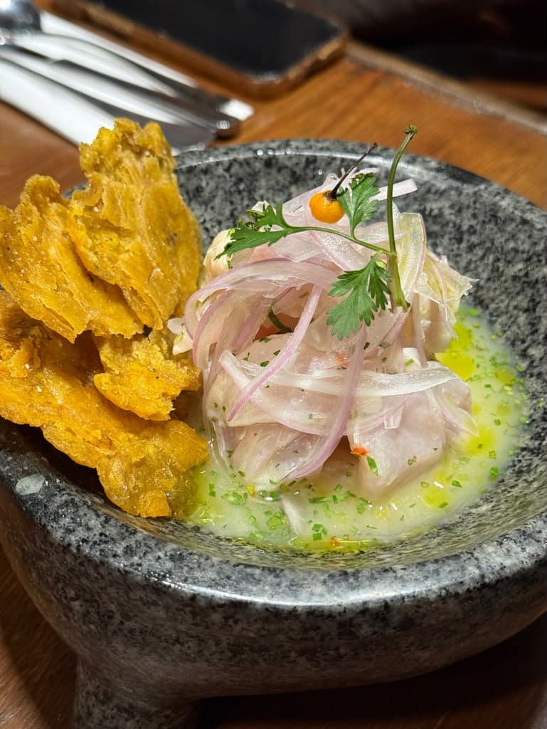 A bowl of Peruvian ceviche with red onion and cilantro beside fried plantain chips