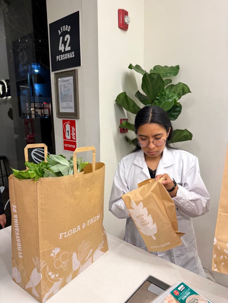 A worker in a white coat bagging fresh greens at the Flora & Fauna grocery in Lima