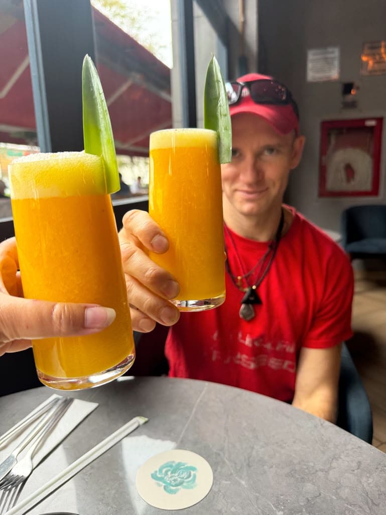 Two tall glasses of fresh orange juice with aloe garnish held up in a toast, Jacob smiling behind them
