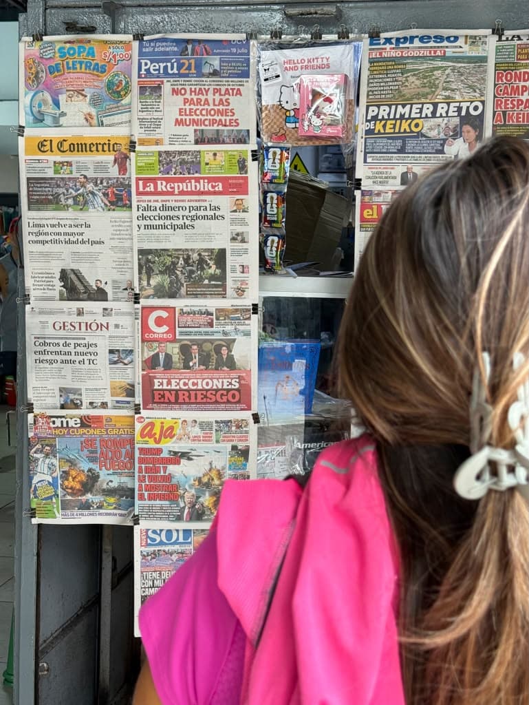 A Lima street newsstand hung with Peruvian newspapers as a passerby reads the headlines