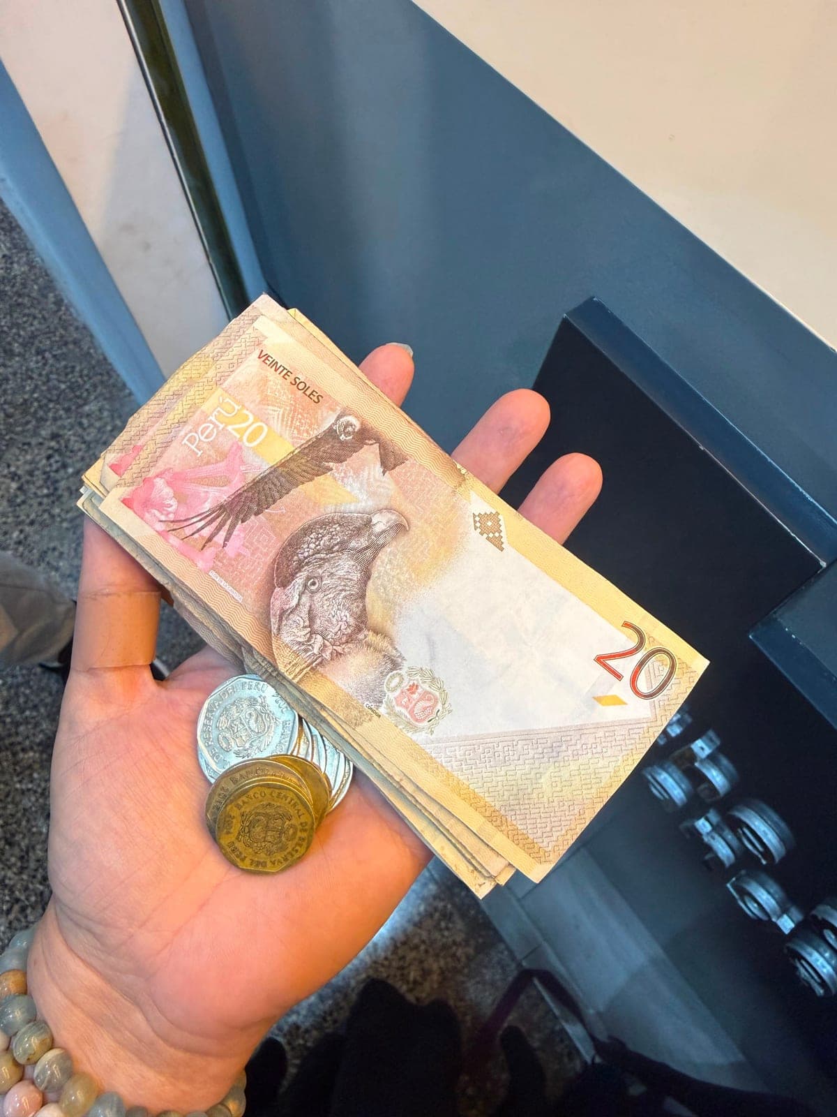 A hand holding a stack of Peruvian soles and coins at the Cusco airport