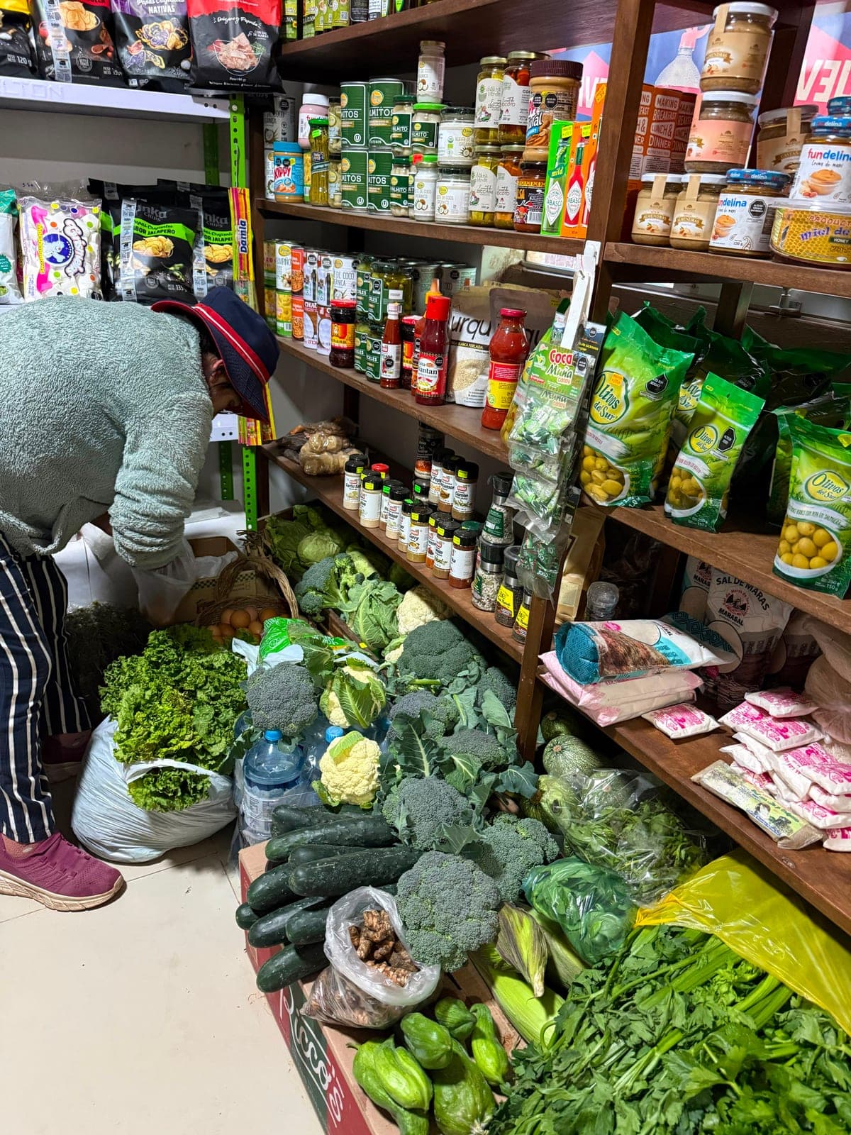 Crates of broccoli, cauliflower, cucumbers and herbs at the small village market, shelves of goods behind